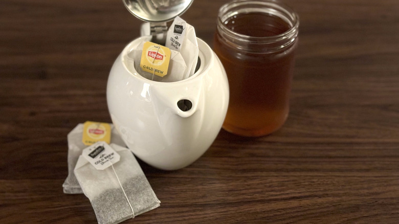 Teapot with tea bags next to more tea bags and clear jar of black tea on table