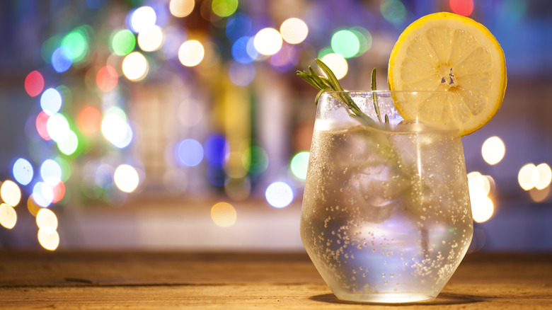 Glass of carbonated water on a bar with blurred lights, rosemary, and garnish