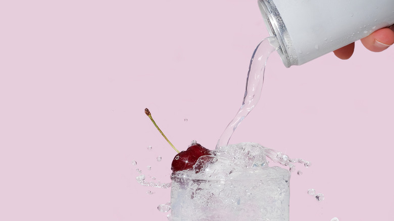 Sparkling water being poured from a white can into a glass with a cherry