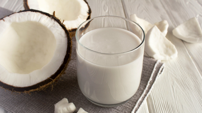 Coconut milk in glass alongside fresh coconut halves