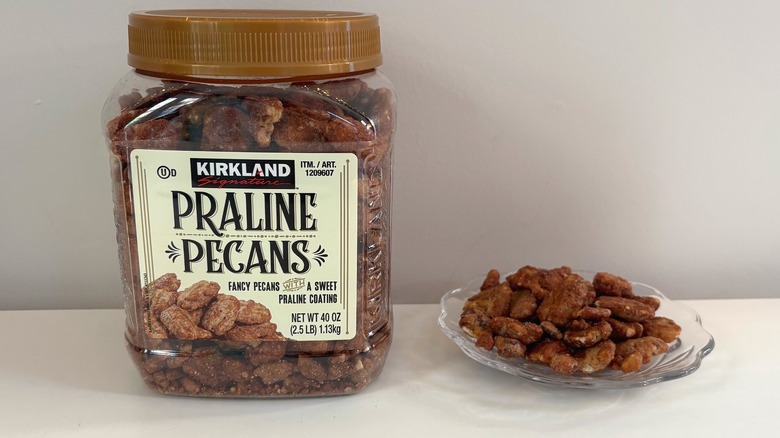 Container of Kirkland praline pecans next to glass plate of praline pecans on white background