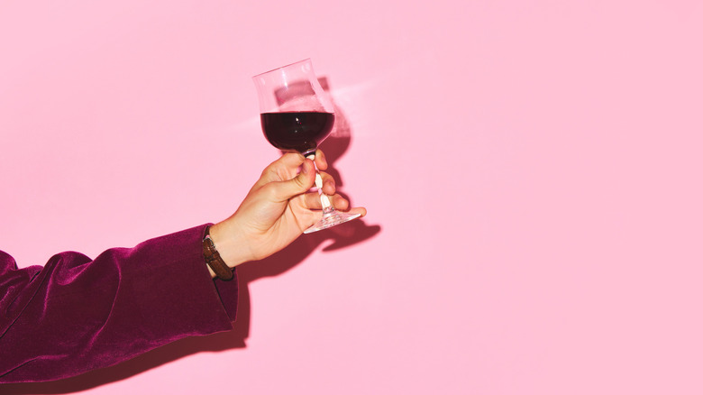 Person holding glass of wine on pink background