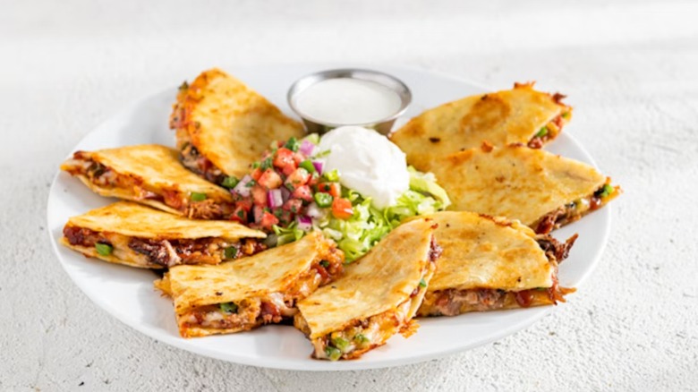 Chili's Brisket Quesadillas, cut into halves, arranged around a pile of shredded lettuce, pico de gallo, and sour cream, plus a metal bowl with dressing, all on a white plate