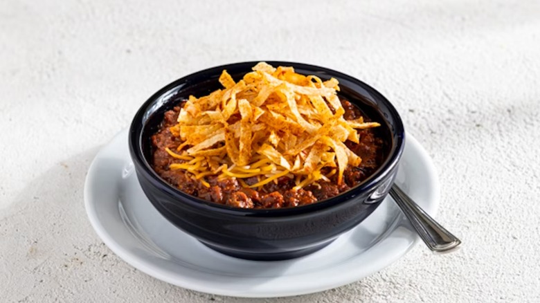 Chili's Bowl of the Original Chili, topped with shredded yellow cheddar and then tortilla chip strips in a black bowl on a white plate