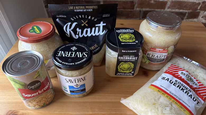 Variety of sauerkraut containers on wooden table with brick background