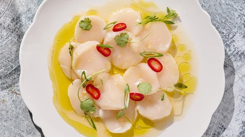 Top-down view of yuzu scallop crudo with white soy on a plate