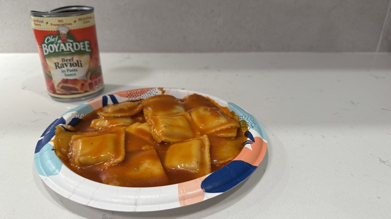 Paper plate on a white counter with raviolis in sauce and an empty can.