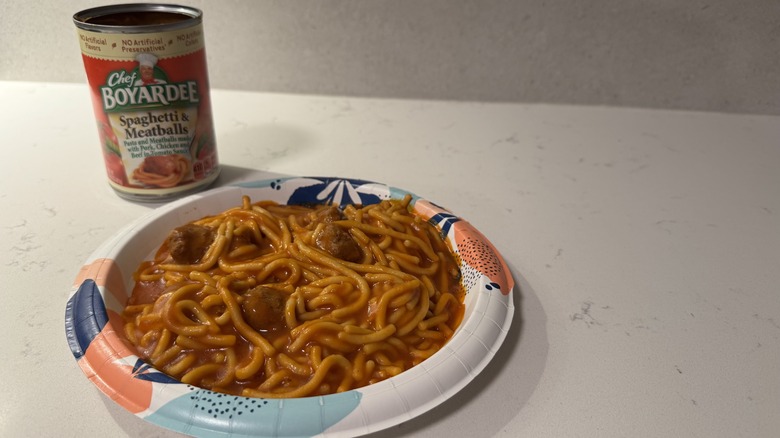 Paper plate of spaghetti on a white counter with meatballs and an empty can.