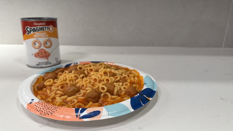 Paper plate on white counter with Spaghettios and meatballs and an empty can.