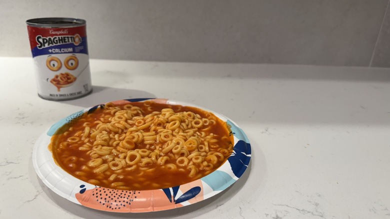 Paper plate on white counter with Spaghettios and an empty can.