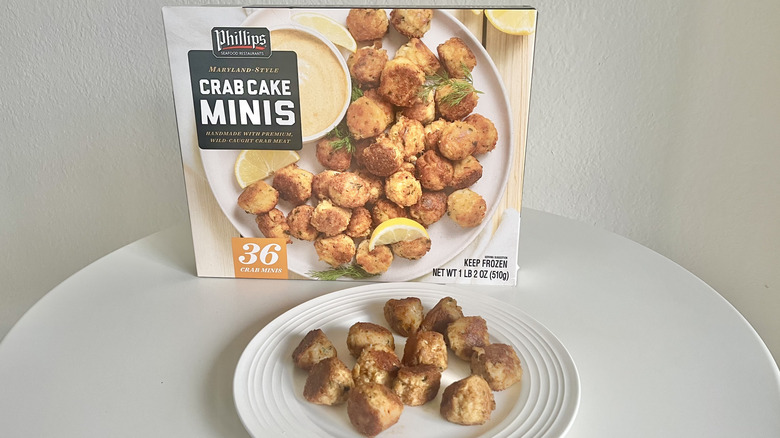 Phillips crab cake minis sit on a plate with the product's packaging behind it.