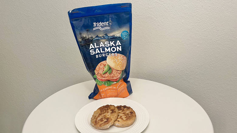 Trident Seafoods salmon burger patties are on a plate with the product's packaging behind it.