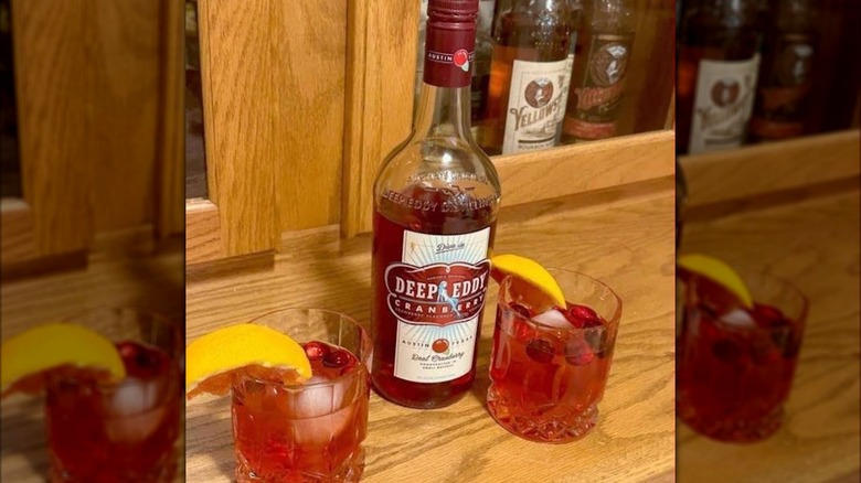 A bottle of Deep Eddy Cranberry Vodka sitting on a wooden countertop, with two cocktails poured.