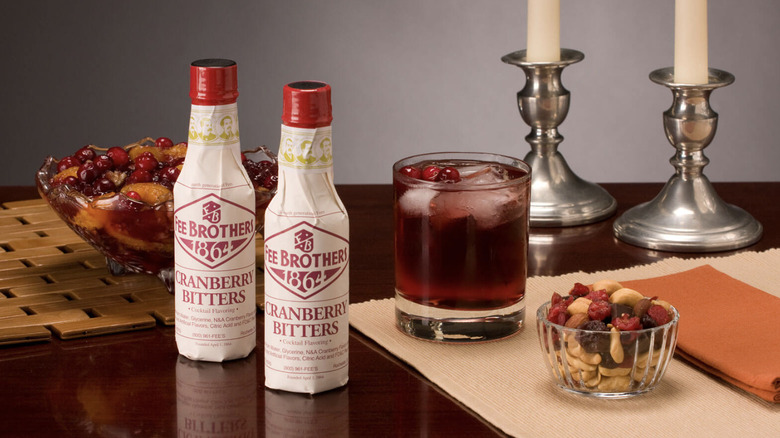 Two bottles of bitters next to a cocktail and bowls of mixed fruit and nuts.