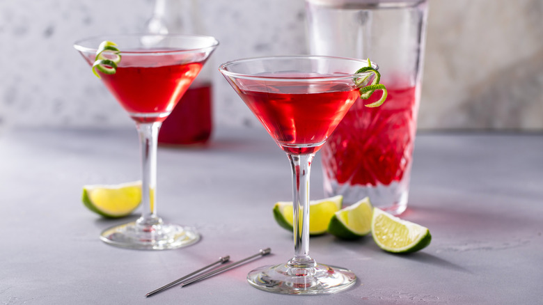 A pair of bright red cranberry flavored cocktails served in martini glasses with lime zest garnishes.