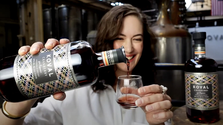 A smiling woman at the Koval distillery pouring a glass of cranberry gin liqueur.