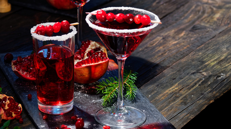 Pair of red drinks in sugar-rimmed glasses, with cranberries and pomegranates, on a wooden table.