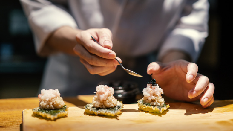 A sushi chef topping a line of fried rice and raw fish with caviar