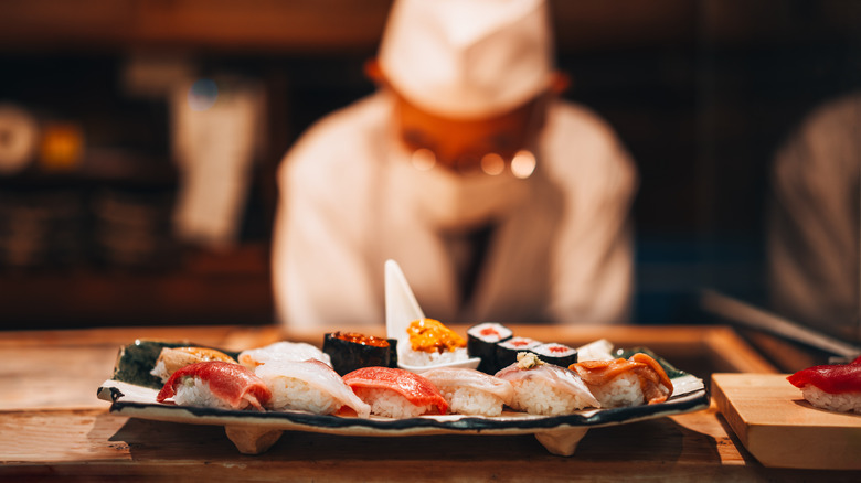 Tray of fresh assorted sushi and sashimi with sushi chef in the background