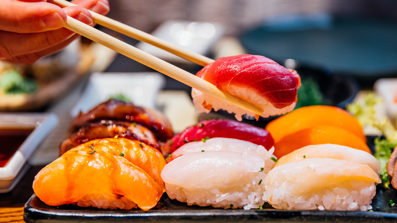 Person holding sashimi with chopsticks above tray of assorted sashimi on restaurant table