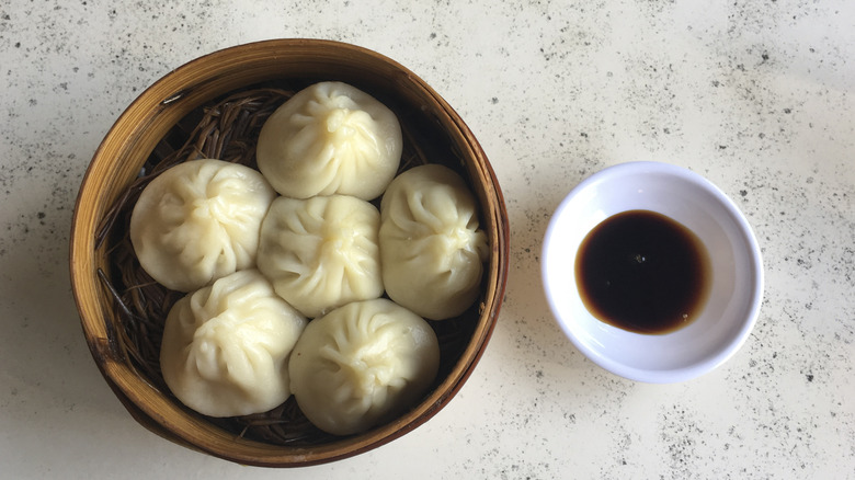 Basket of soup dumplings and dipping sauce on table