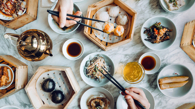 Two pairs of chopsticks grabbing from an assortment of dim sum dishes on the table