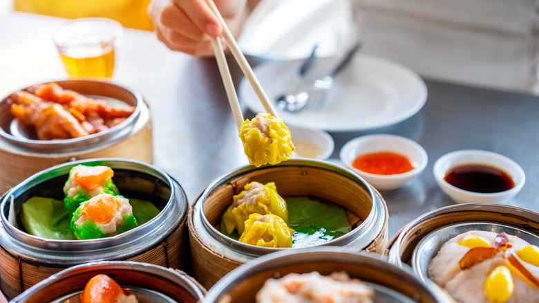 Chopstick picking up siu mai from table full of dim sum