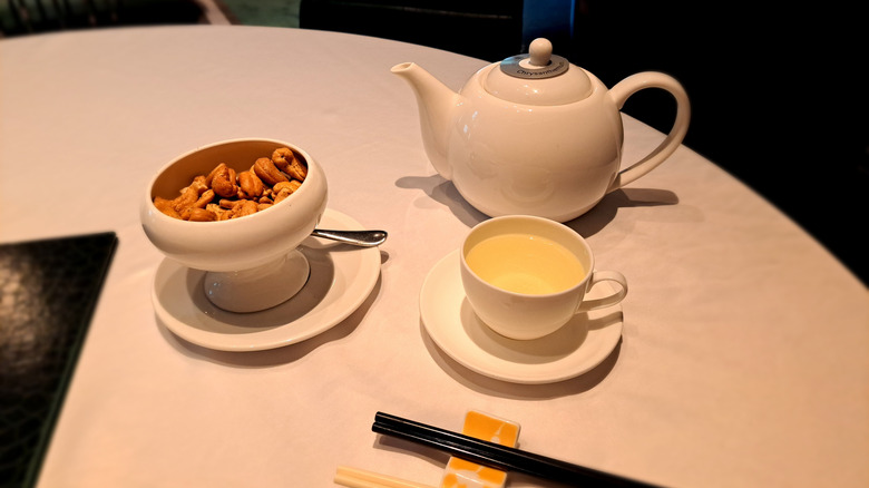 Pot of tea, teacup, and bowl of cashews on restaurant table