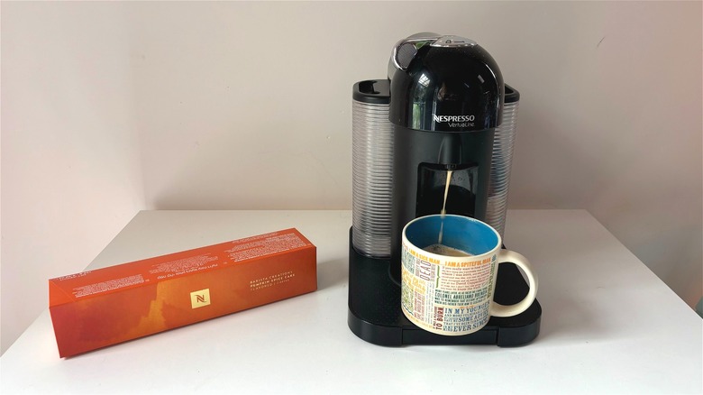 Box of Nespresso pumpkin spice cake pods next to Nespresso machine brewing coffee