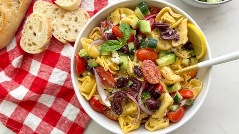 Top-down view of tortellini Greek salad in a white bowl with ciabatta bread 