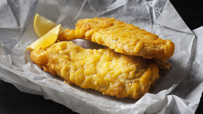 Two pieces of fried fish and lemon on white parchment paper