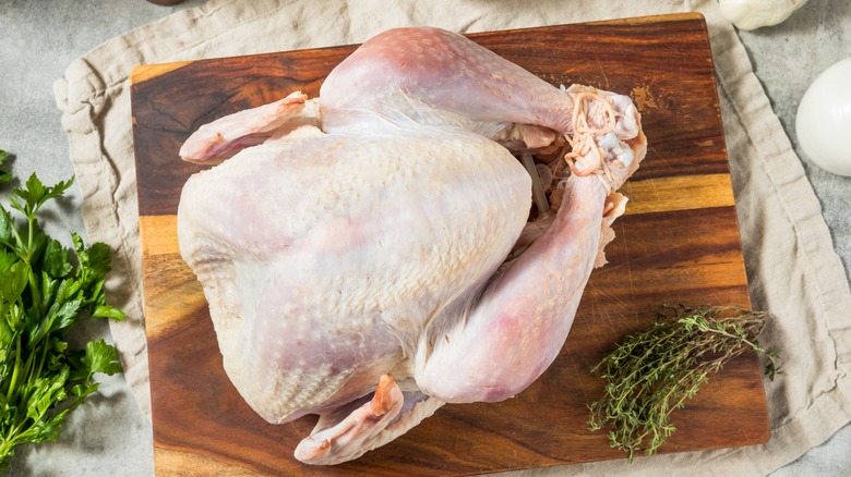 Whole, raw turkey on wooden cutting board surrounded by herbs