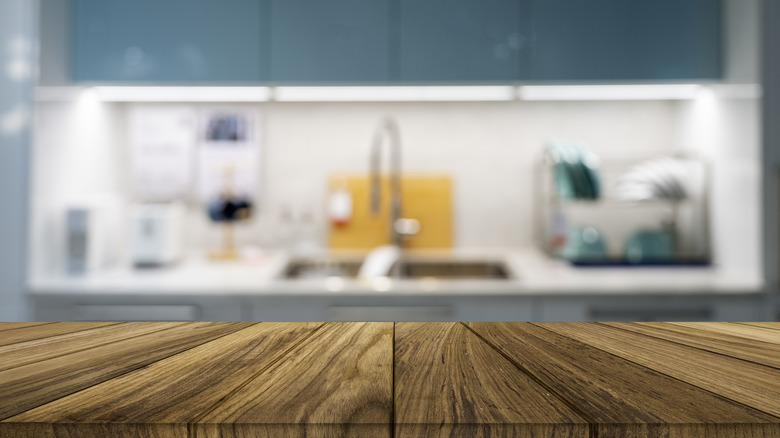 Wooden kitchen counter with blue walls and sink in the background