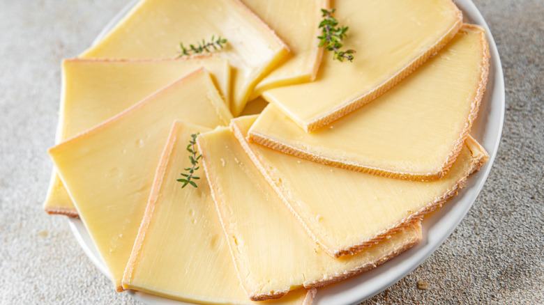 sliced raclette cheese layered on a white plate and decorated with thyme sprigs