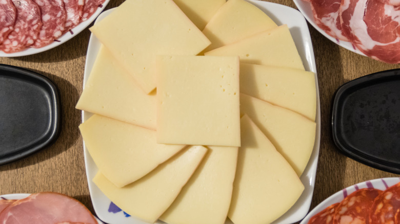 sliced raclette cheese layered on a plate surrounded by various types of charcuterie