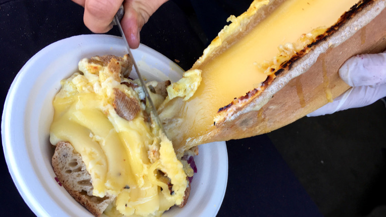 scraping grilled raclette over crusty bread in a white bowl