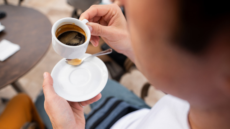 Person holding a small coffee cup and saucer