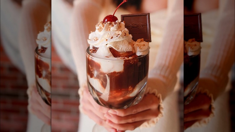 Hands holding hot fudge sundae