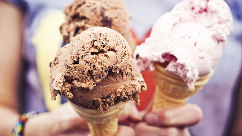 Three hands holding cones of ice cream in chocolate and strawberry flavors