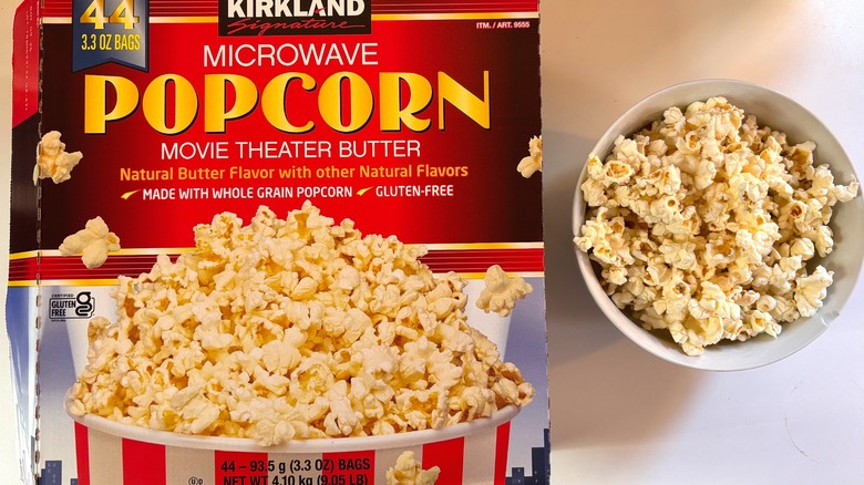 Box of Kirkland microwave popcorn next to white bowl of popcorn on white table