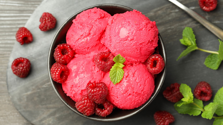 Bowl of raspberry sorbet in bowl with raspberries and mint leaves