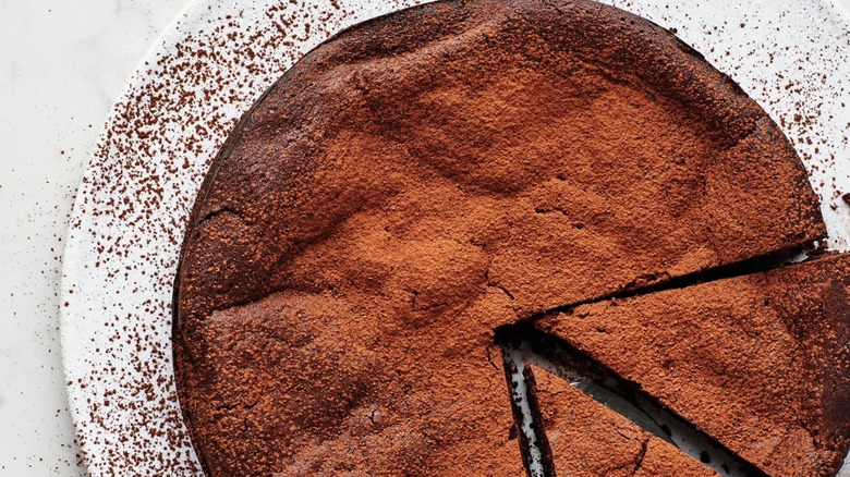 Flourless chocolate cake on white serving tray with two slices cut