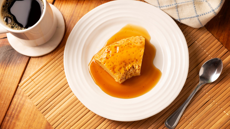 Slice of flan on plate with bites taken out next to cup of coffee