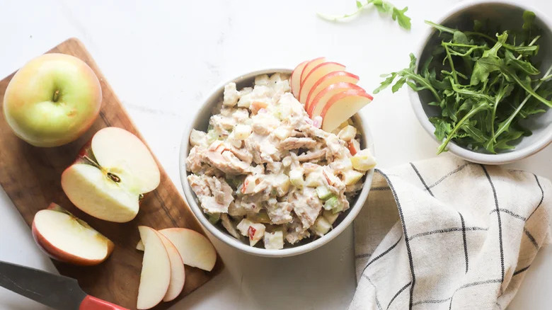 Bowl of tuna salad next to apple and greens