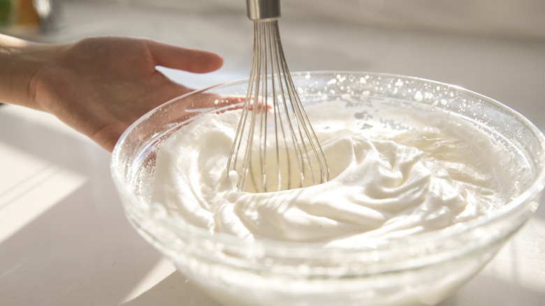 Stirring whipped cream with a whisk in a glass bowl