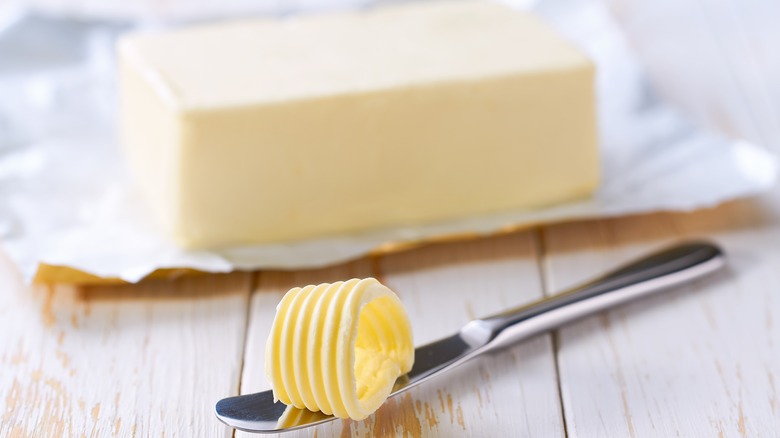 Block of butter with knife on wooden table