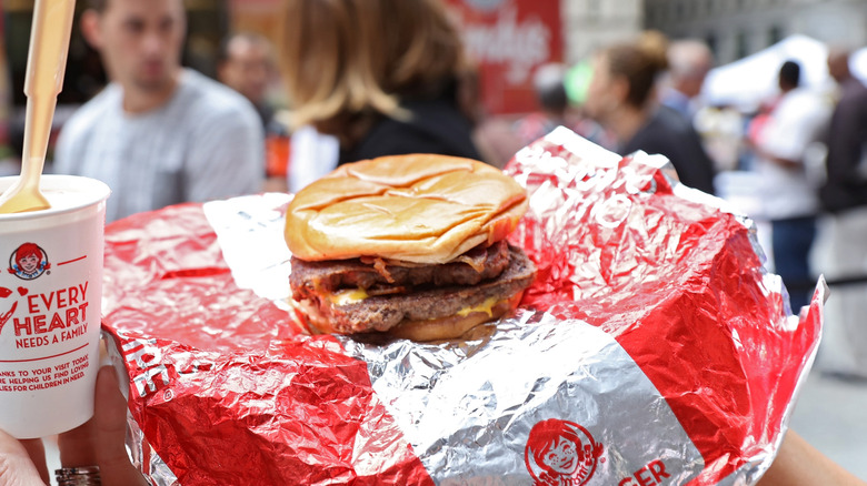 Hands holding Wendy's Baconator burger on top of its foil wrapper