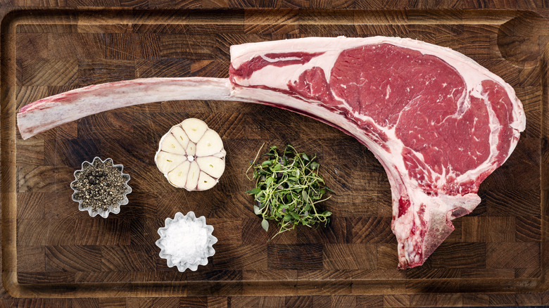 raw tomahawk steak on cutting board with seasonings