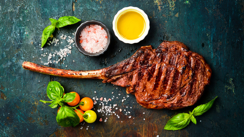 grilled tomahawk steak on slate with condiments and herbs