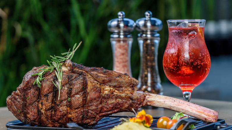 grilled tomahawk steak with salt and pepper shakers in the background and a glass of wine